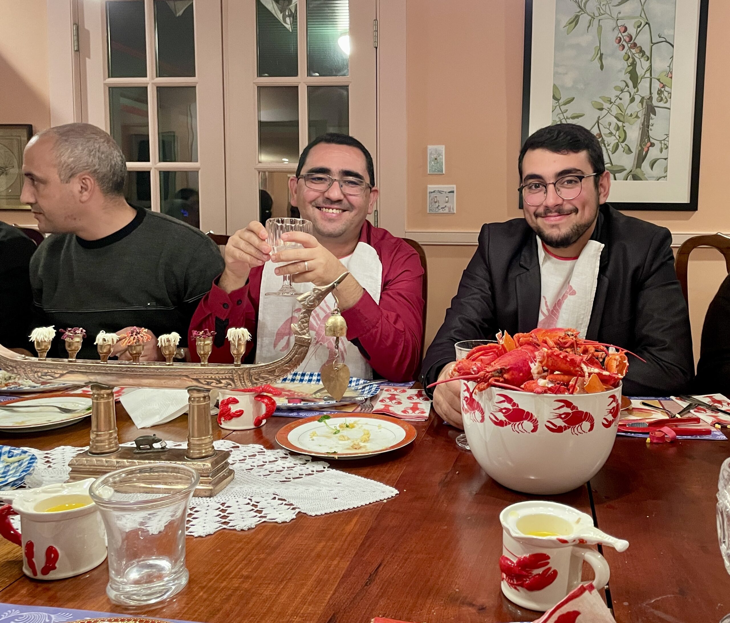 two men smiling at dining room table with a bucket full of lobster shells