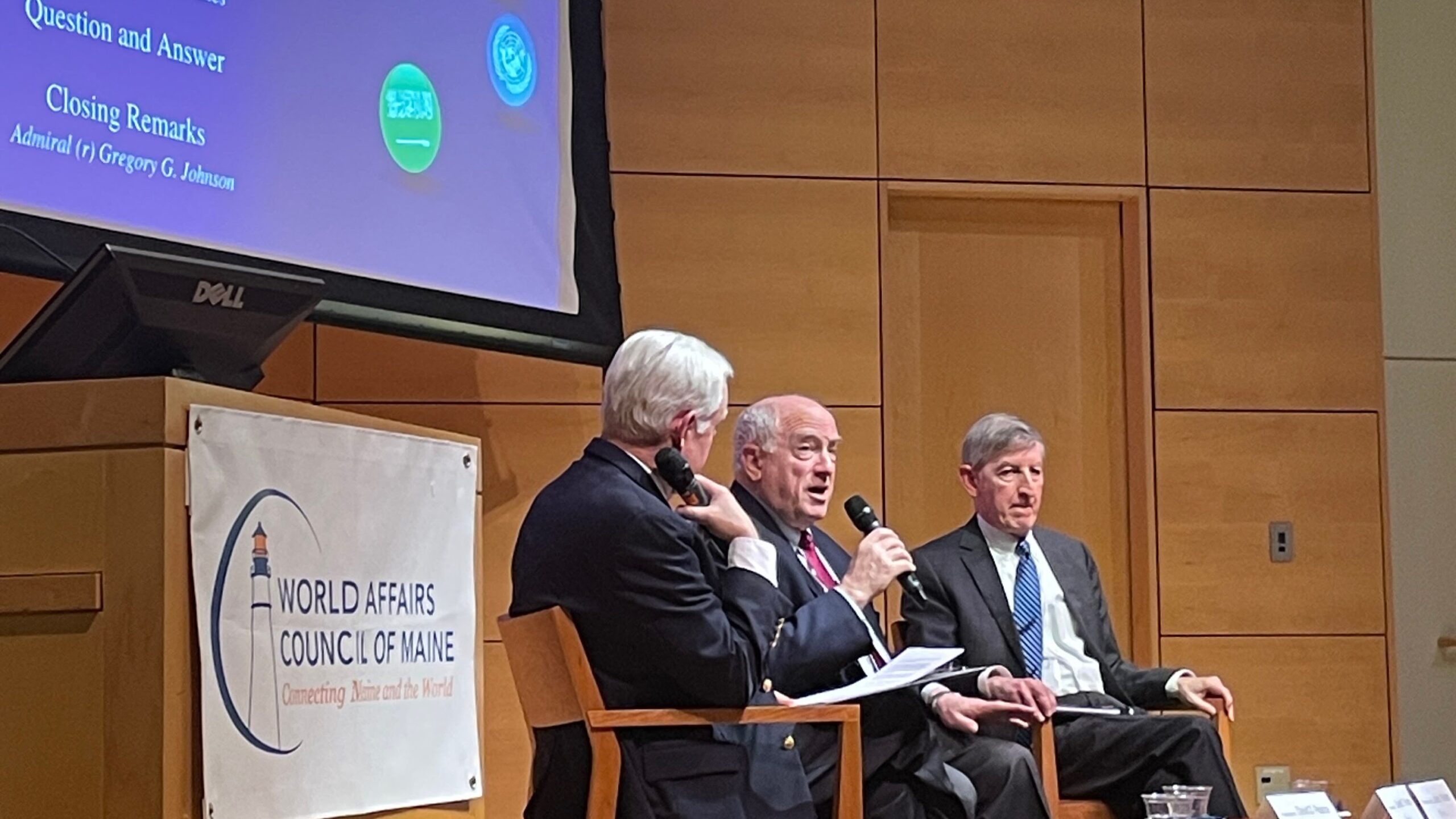 three men sitting on stage presenting